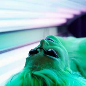 woman sitting in tanning bed which could be a Basal Cell Carcinoma Cause