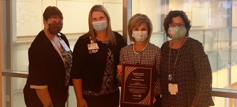 Four masked women stand side by side with the PFAC Award of Excellence plaque.