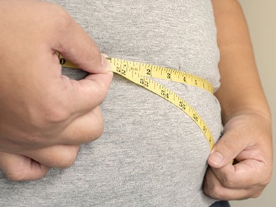 overweight person with tape measure over stomach