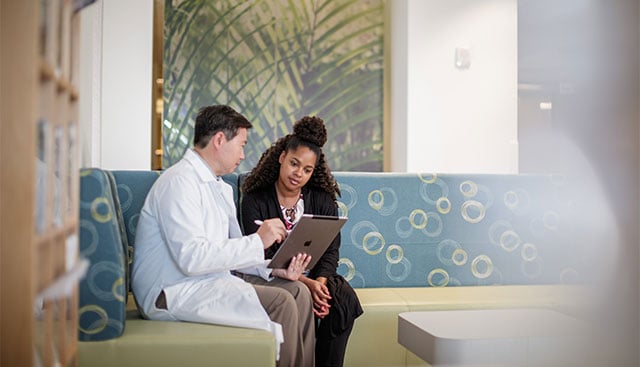 An oncologist sitting on a couch showing a patient information on an ipad.