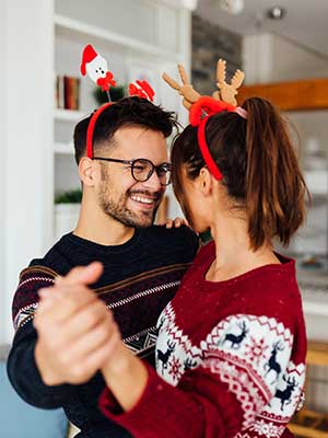 Man and woman dance in their home while wearing holiday sweaters