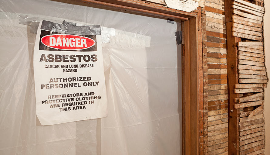 A danger asbestos warning sign hanging on a doorway inside an older house.