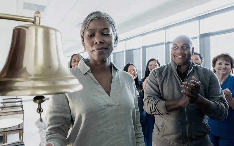 A patient rings a bell with family and staff around them